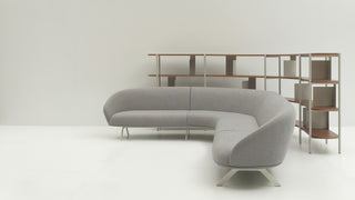Gray curved sofa in a minimalistic room with a bookshelf.