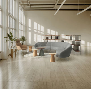 Modern office space with a gray sectional sofa, wooden tables, and large windows.