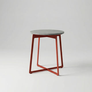 Small round table with a concrete top and red metal legs on a light gray background