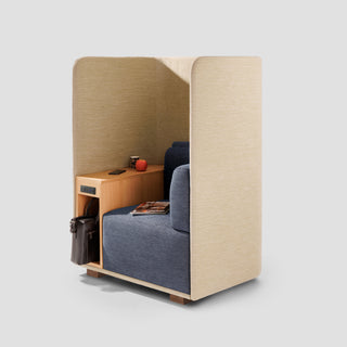 Small office pod with a blue seat, wooden side table, and beige walls on a light gray background.