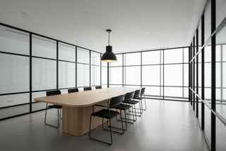 Modern conference room with a long wooden table and black chairs in front of large windows.