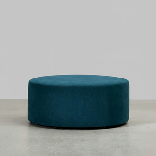 Teal ottoman on a light gray floor with a white wall background