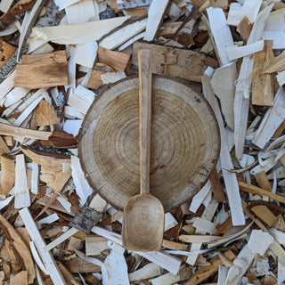Large wooden serving spoon on wood slice and shavings